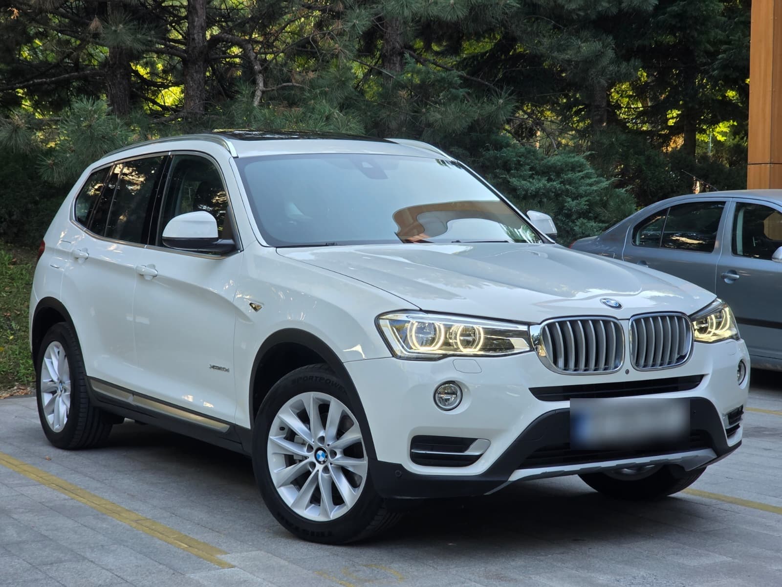 BMW X3 alb, parcat în fața unor pini